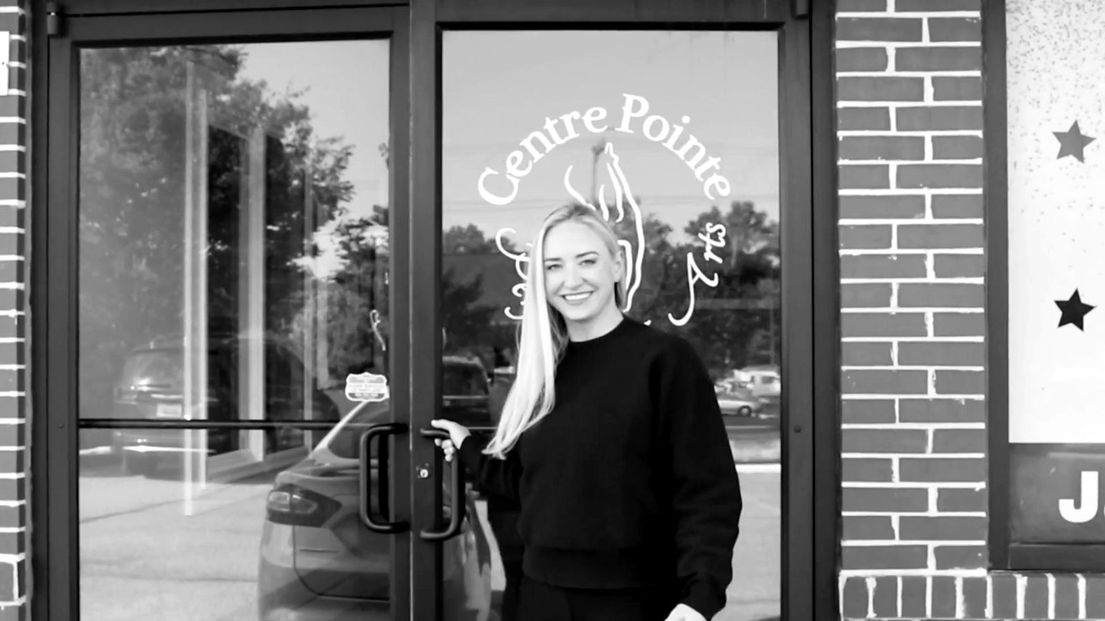 A Centre Pointe staff member smiling at the studio&rsquo;s front door, the logo painted on the glass