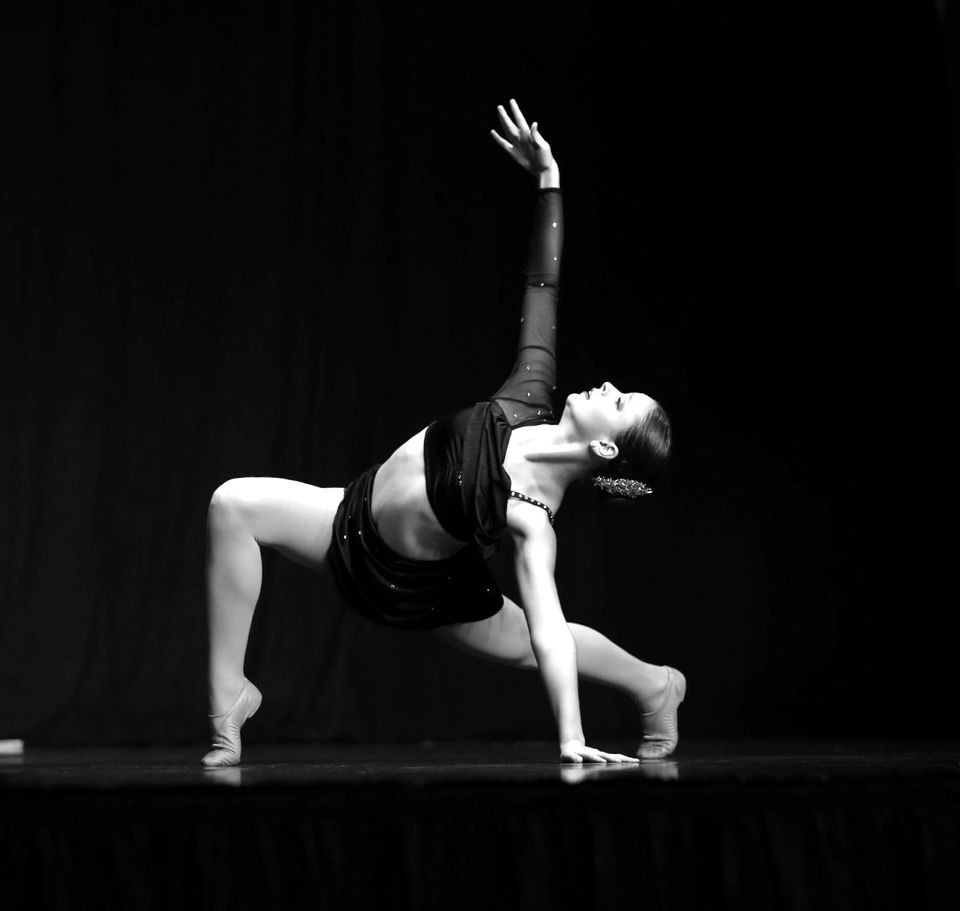 A dancer in a black costume in a deep lunge on a dark stage
