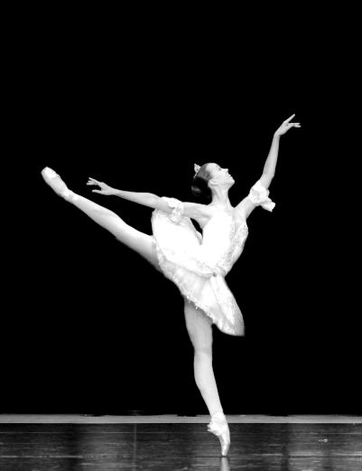 A ballerina in a white tutu balancing in arabesque on stage
