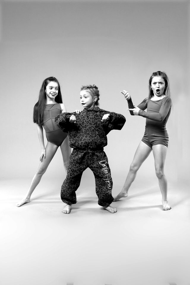 Three dancers in red costumes and a leopard-print jumpsuit striking a pose
