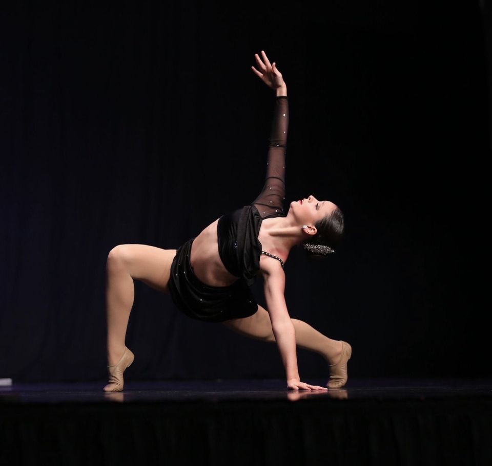 A dancer in a black costume in a deep lunge on a dark stage