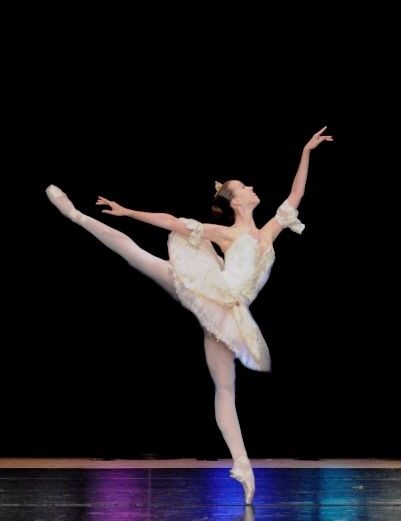 A ballerina in a white tutu balancing in arabesque on stage
