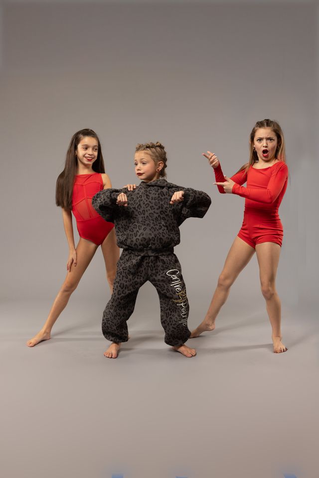 Three dancers in red costumes and a leopard-print jumpsuit striking a pose